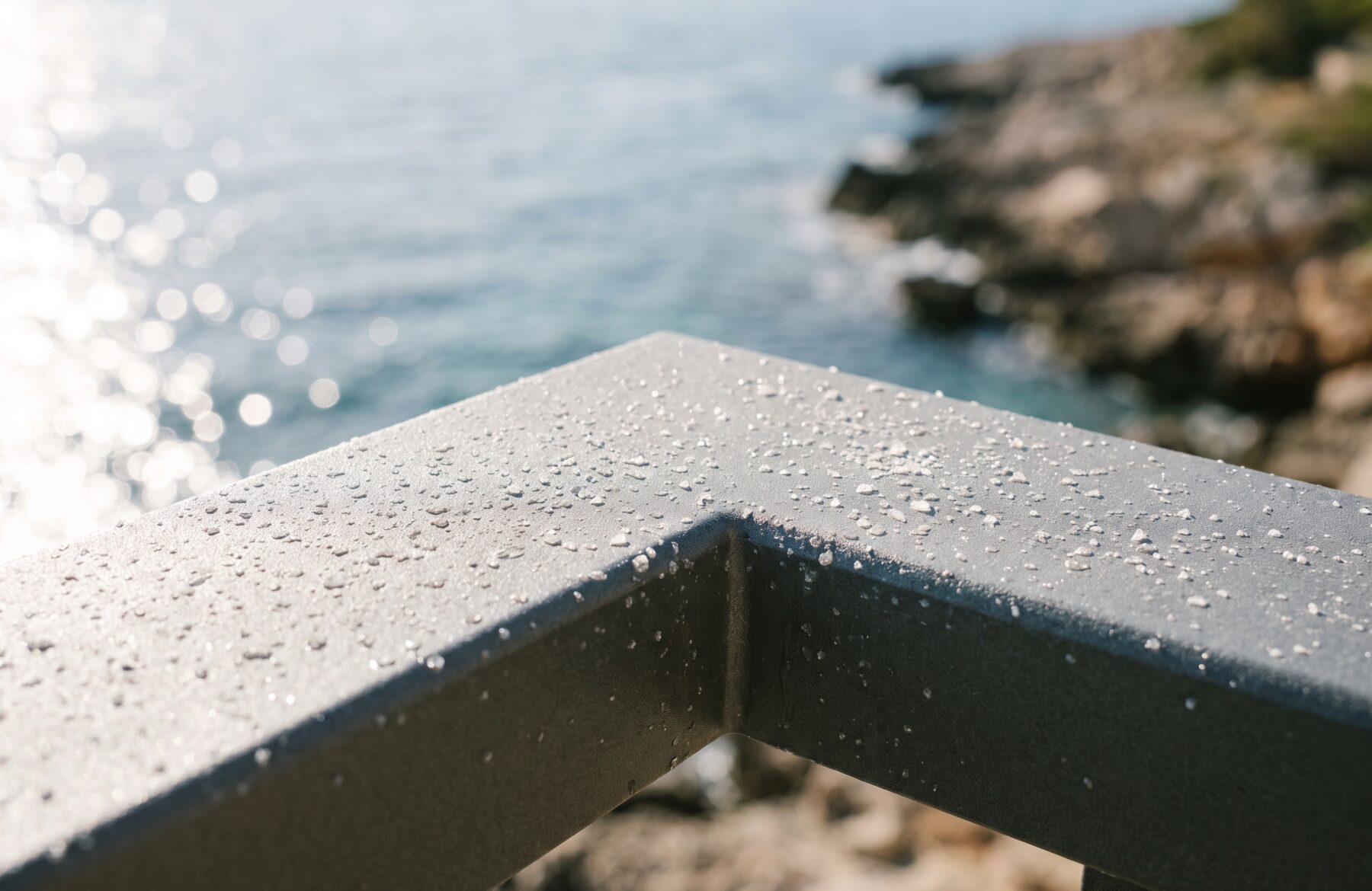 Angle d’un cadre en aluminium anthracite perlé de fines gouttelettes, la mer floue en arrière-plan