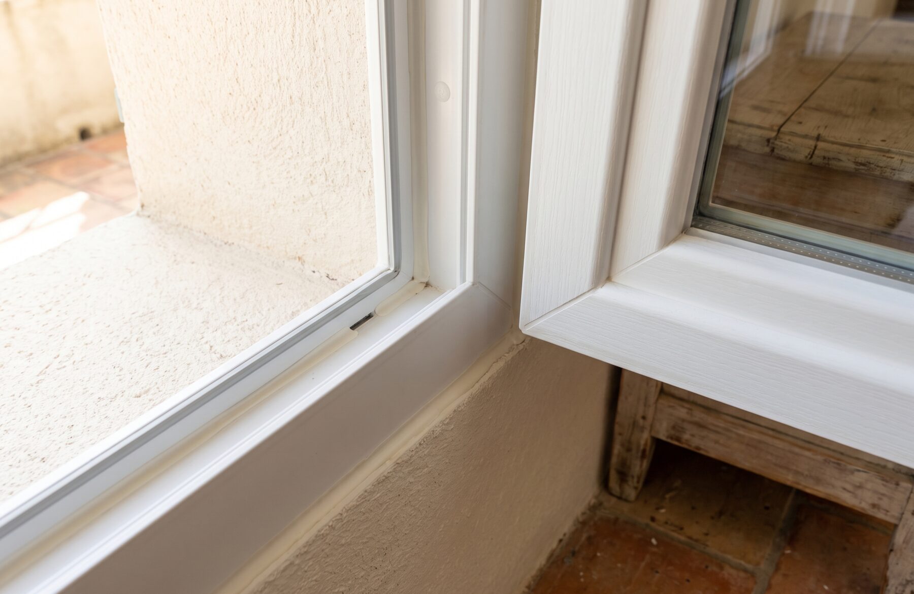 Angle d’une fenêtre PVC blanche ouverte : dormant, jonction avec le mur enduit et appui