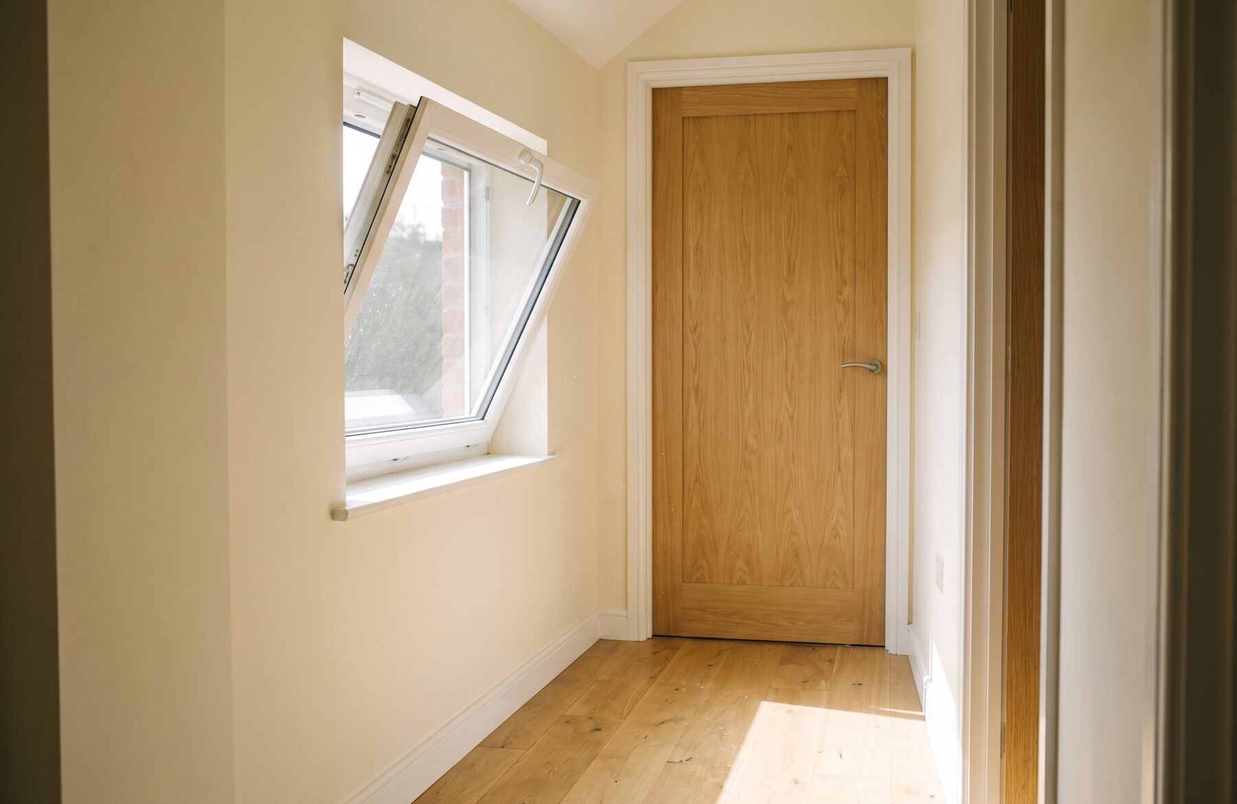Fenêtre basculée en soufflet dans un couloir lumineux, à côté d’une porte en chêne