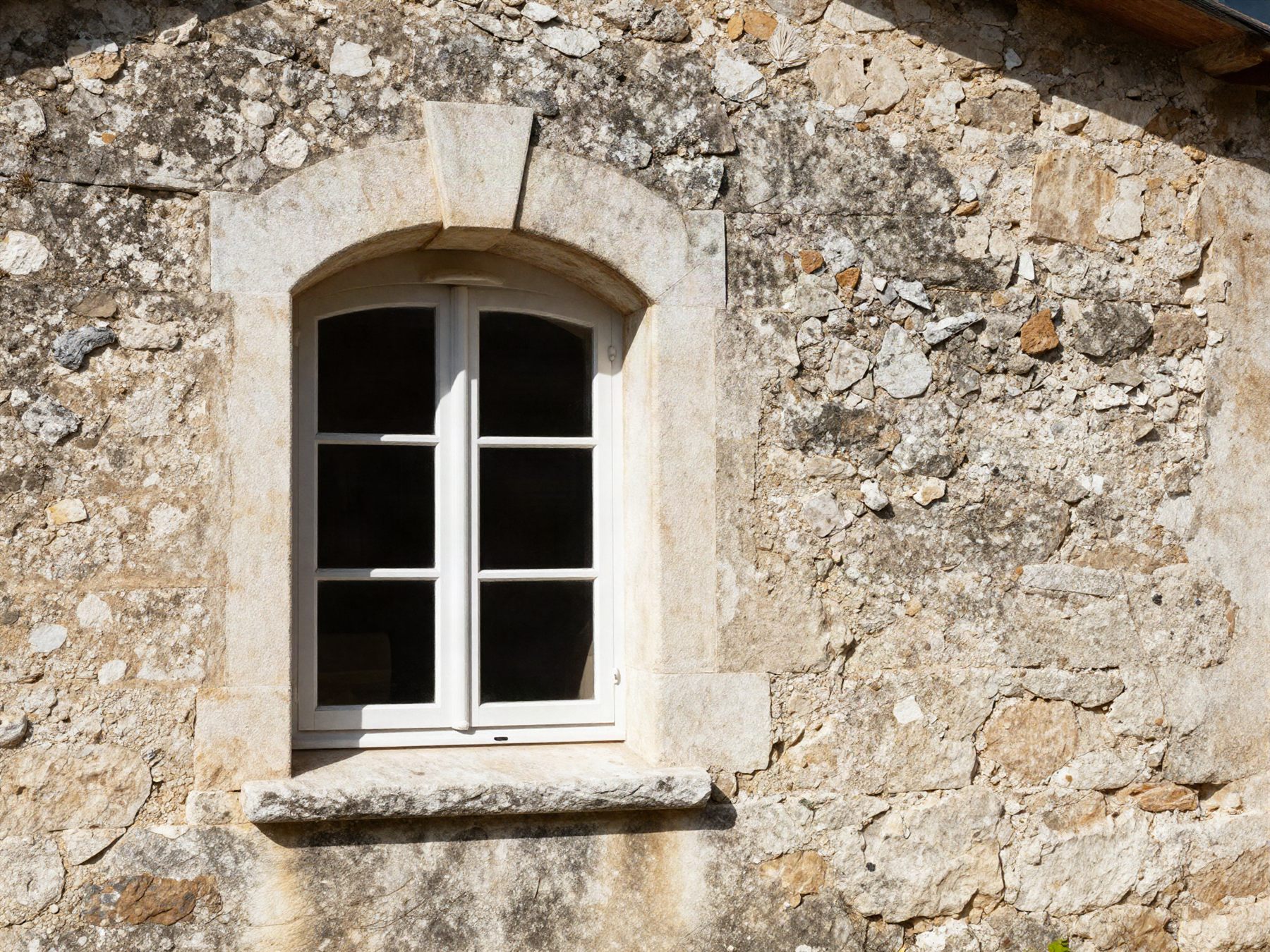 Fenêtre cintrée sur mesure posée dans un mur de pierre d'une maison de village de l'Hérault